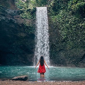 Eine Frau in einem roten Kleid vor einem Wasserfall. Es symbolisiert die Kraftquellen im Focusing